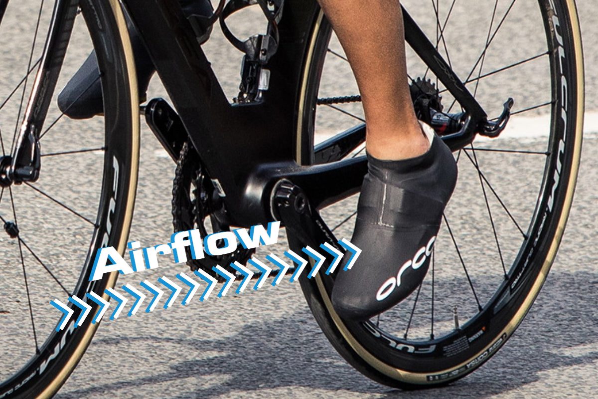 Unterschenkel eines Radfahrers in der Trittbewegung. Er trägt schwarze Überschuhe über seinen Radschuhen