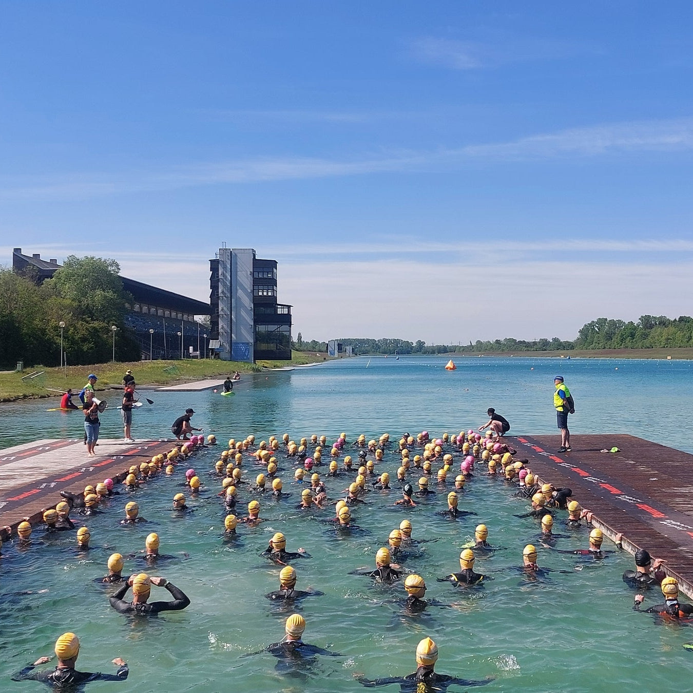 Triathleten mit gelben Badekappen warten im Wasser der Ruderregattastrecke Oberschleissheim auf den Start