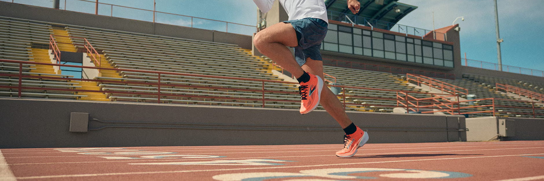 Ein Läufer mit roten Brooks Laufschuhen auf einer Tartanbahn in dynamischem Tempo auf der Zielgeraden. Ansicht von schräg vorn