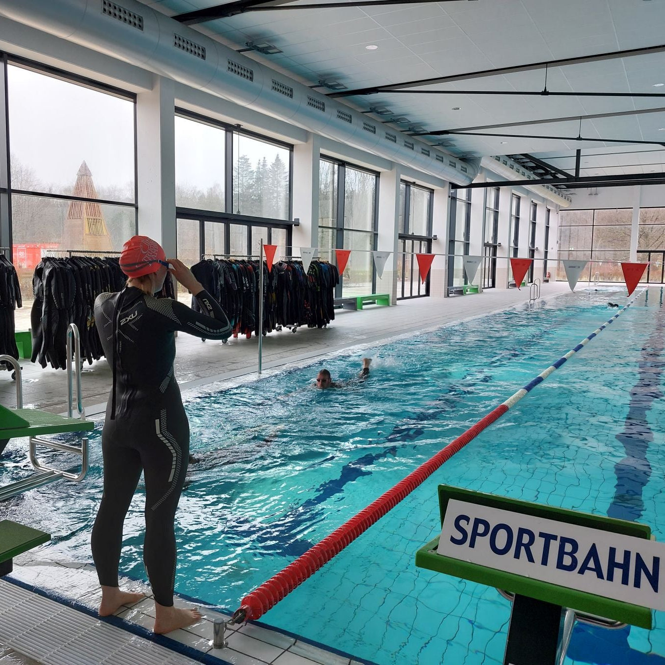 Eine Schwimmerin beim Neoprentest. Sie steht am Beckenrand einer Sportbahn und macht sich bereit, ins Wasser zu springen