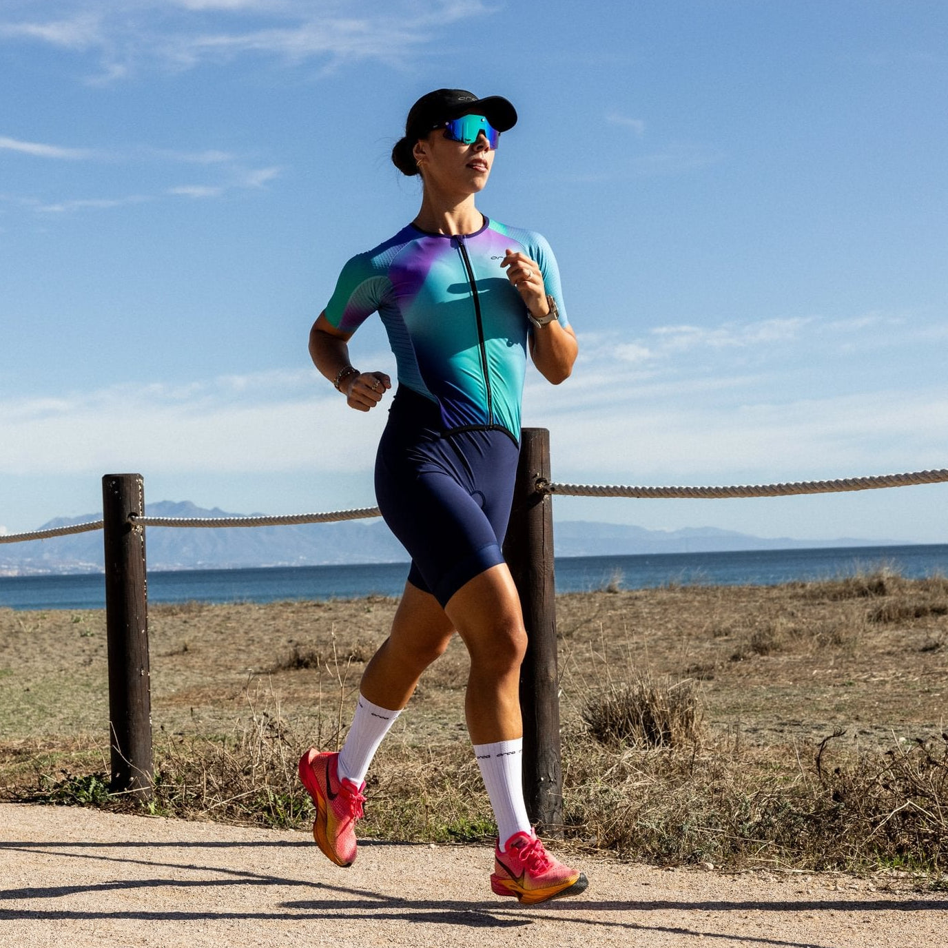 Eine Frau im hellblauen Triathlon-Einteiler läuft an einer Strandpromende entlang