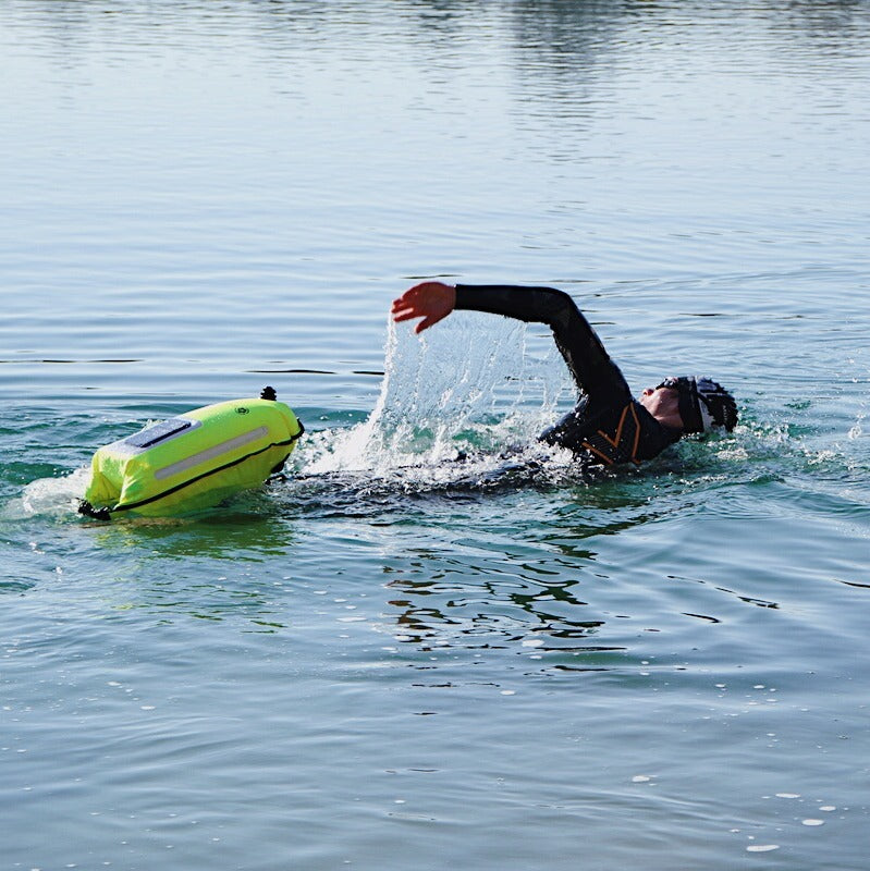 Ein Mann im Neoprenanzug schwimmt im See und zieht eine neongelbe Schwimmboje hinter sich her