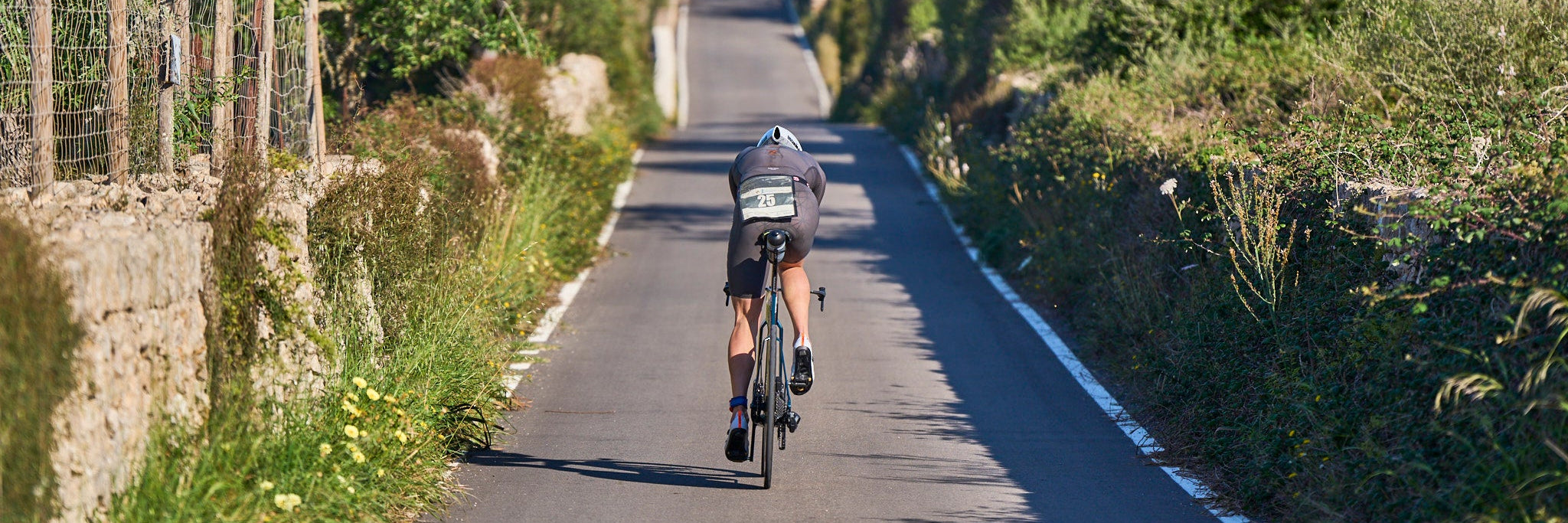 Ein Triathlet auf seinem Fahrrad von hinten fährt auf einer schmalen Straße durch das mallorcinische  Hinterland