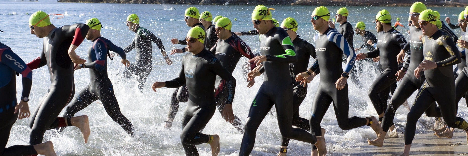Viele männliche Triathleten rennen im Neoprenanzug ins Meer